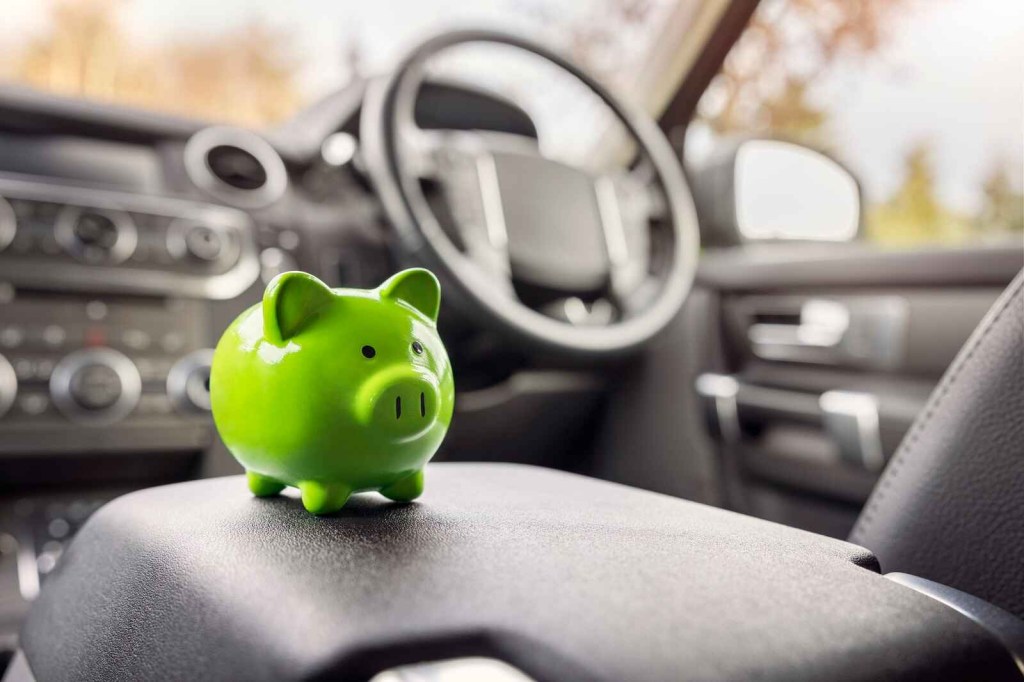 A green piggy bank sits on the center console of a car interior with steering wheel in background