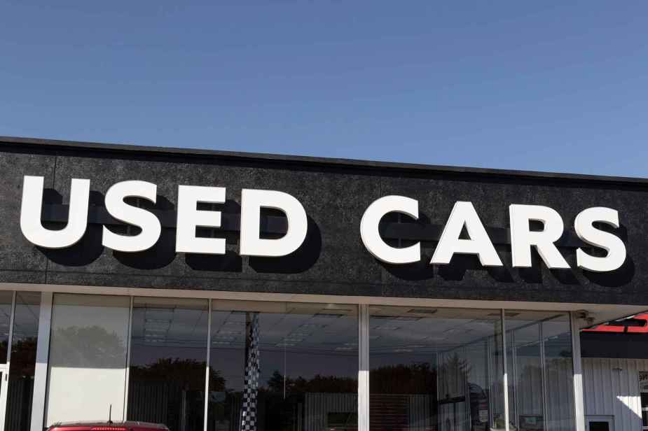 Backlit lettering spelling "Used Cars" is shown on the front of a car sales building