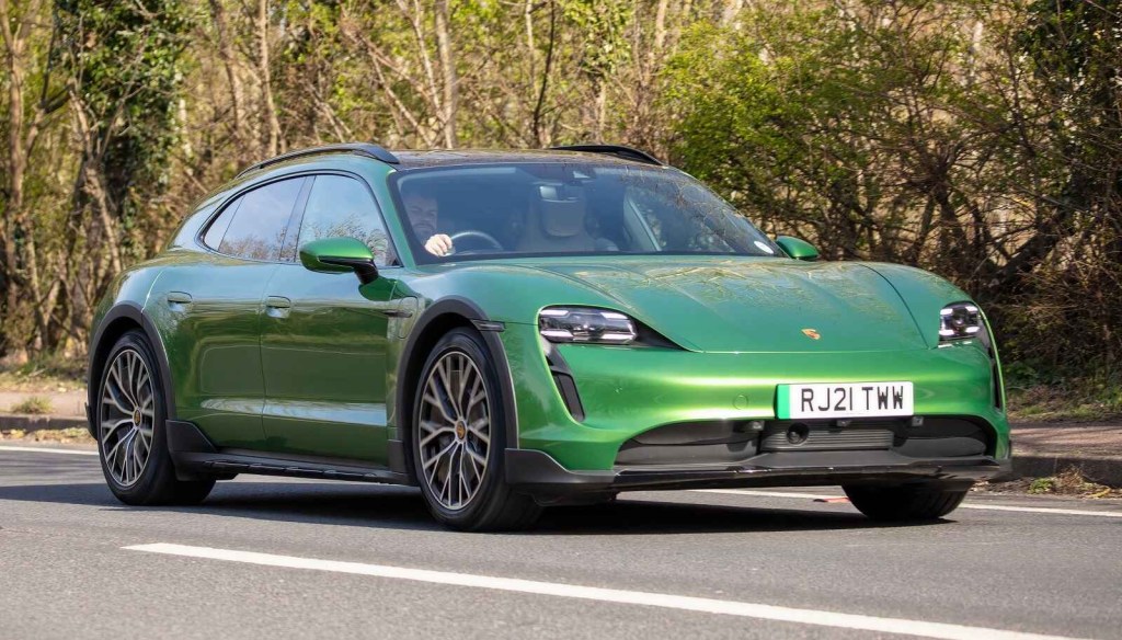 A green Porsche Taycan Turismo driving on a paved road right-hand steering wheel