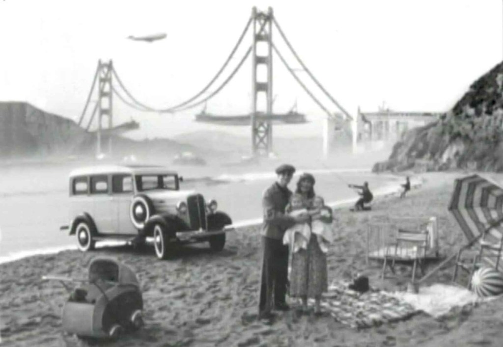 A 1936 Chevrolet Suburban parked at the beach with a couple holding two babies bridge in background