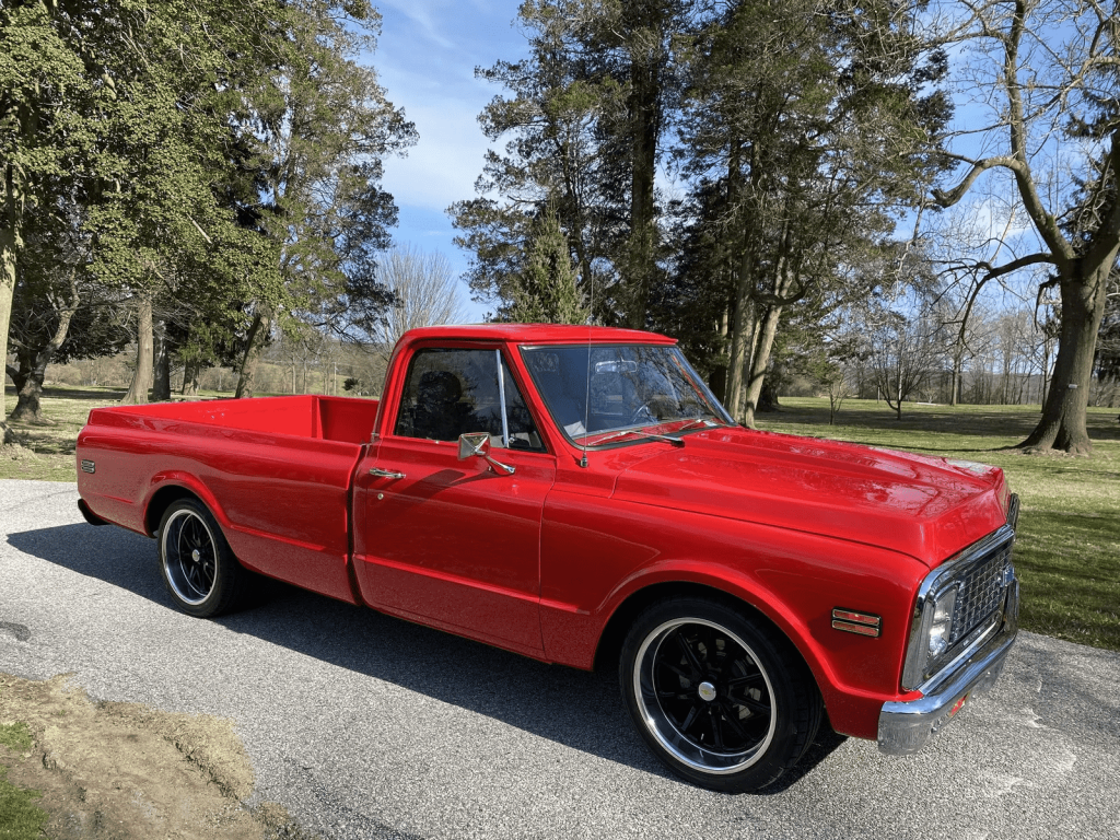 A red 1971 Chevrolet C10 pickup truck which was the truck featured in the film 'Groundhog Day' parked at right front angle view on a paved road with trees in background