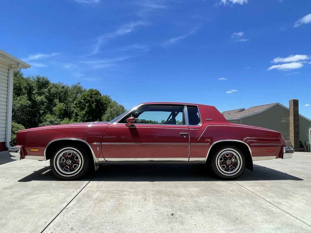 A red 1980 Oldsmobile Cutlass Supreme coupe parked in full left profile view with blue sky in background