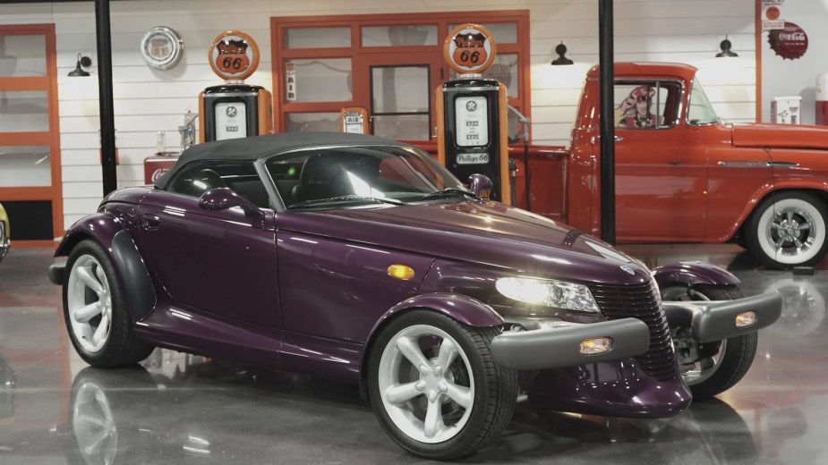 A purple Plymouth Prowler roadster in a garage full of classics