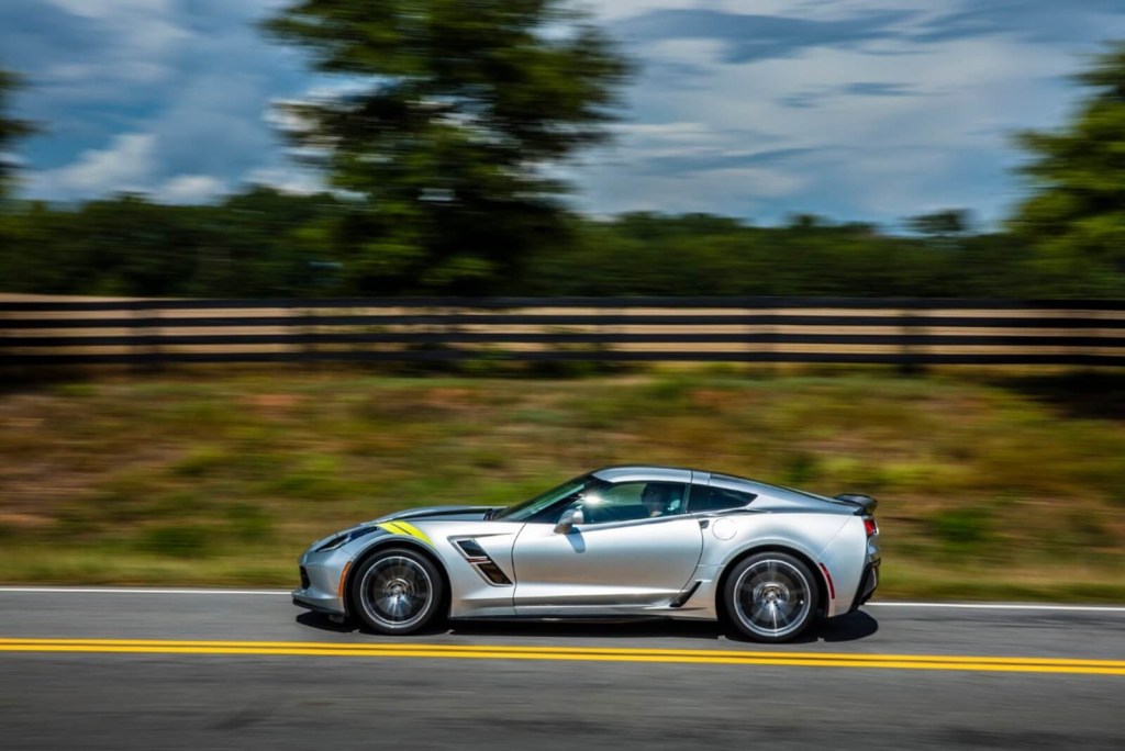 A silver Chevrolet Corvette C7 sports car flogs its V8 up a country road. 