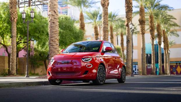 A red 2024 FIAT 500e drives past palm trees.