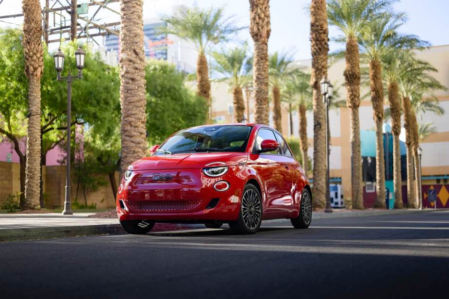 A red 2024 FIAT 500e drives past palm trees.