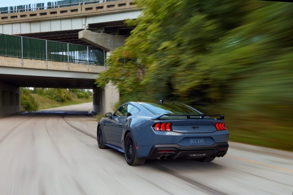 A blue 2024 Ford Mustang GT, a sports car with adaptive cruise control, blasts down a city street. 