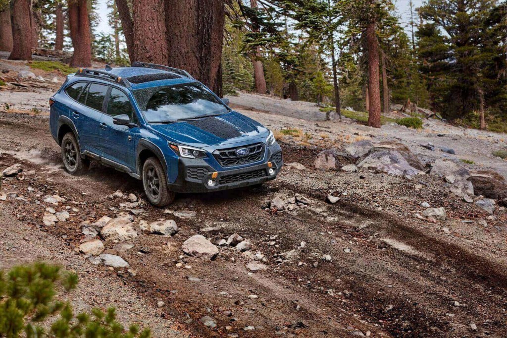A blue 2024 Subaru Outback, one of the best cars for dog owners, drives down a hill. 