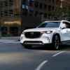 A white 2024 Mazda CX-90 PHEV SUV turning a corner on a paved downtown street