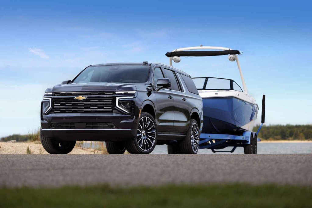 A black 2025 Chevrolet Suburban shown parked in left front angle view towing a blue and white boat
