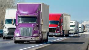 Purple semi-truck at the head of a convoy on the highway
