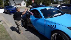 8-year-old high-fives the driver of a blue sports car during a parade.