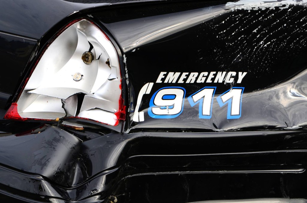The "Emergency 911" decal on the smashed fender of a crashed police car.