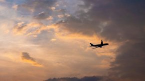 The silhouette of a jet airplane flying across a sunset.