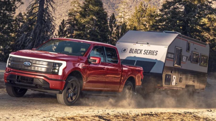 Red Ford F-150 Lightning electric truck towing a trailer on a dirt trail.