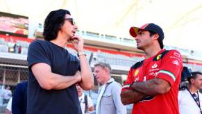 Adam Driver and Carlos Sainz chat in the pits at an F1 race.
