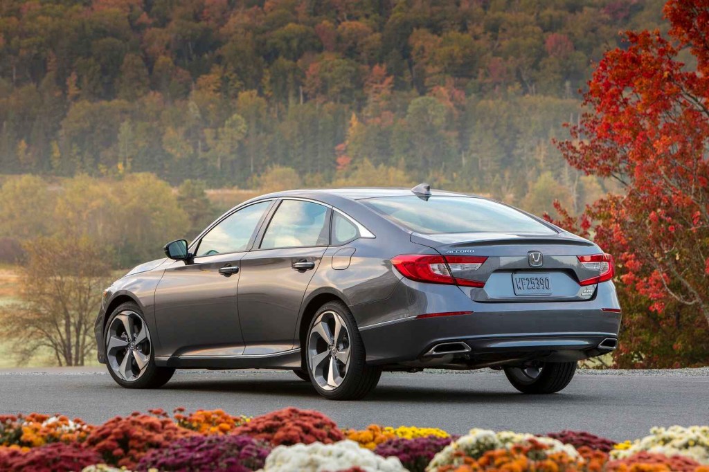 A grey 2018 Honda Accord Touring 2.0T is shown parked in left rear angle view with fall colored trees in the background