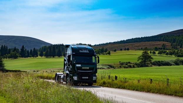 Green semi truck with no trailer driving through the Scottish countryside, powered by Whisky byproducts.