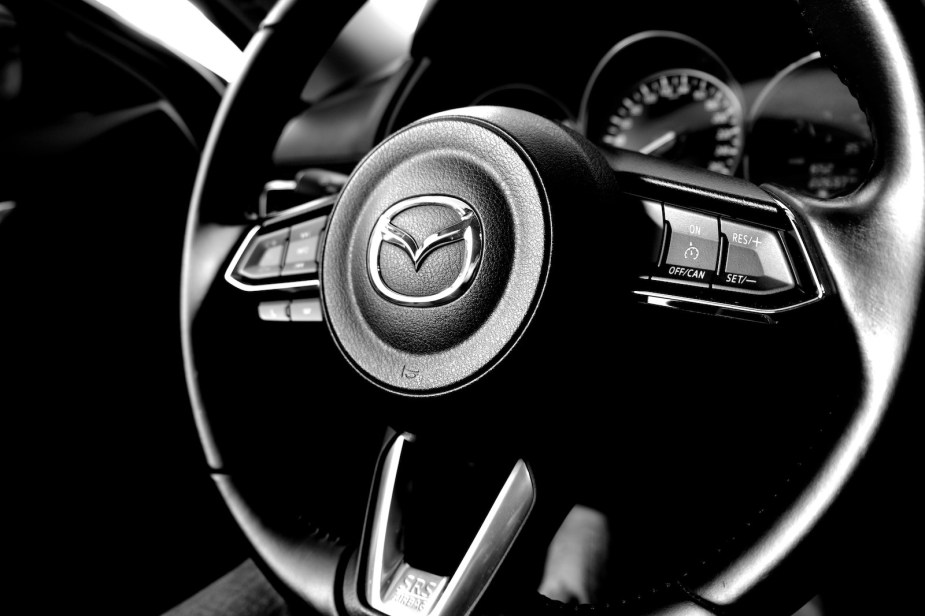 The Mazda logo on the steering wheel of a car.