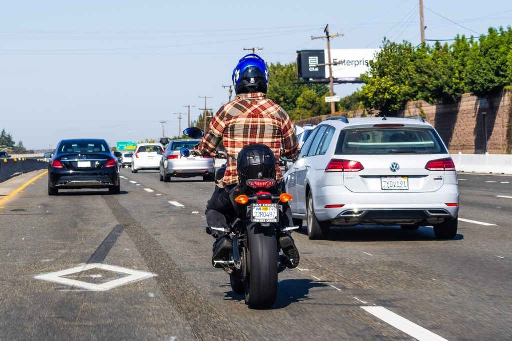 A rider in motorcycle safety equipment rides on the highway as a driver practices adopting a rider. 