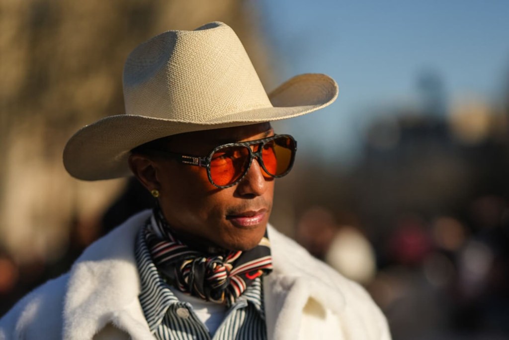 Pharrell Williams, a celebrity with a Tesla Cybertruck, poses in a cowboy hat and rust colored glasses. 