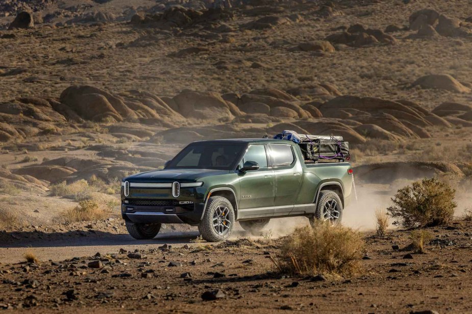 A green Rivian electric pickup truck driving down a dirt 4x4 road.