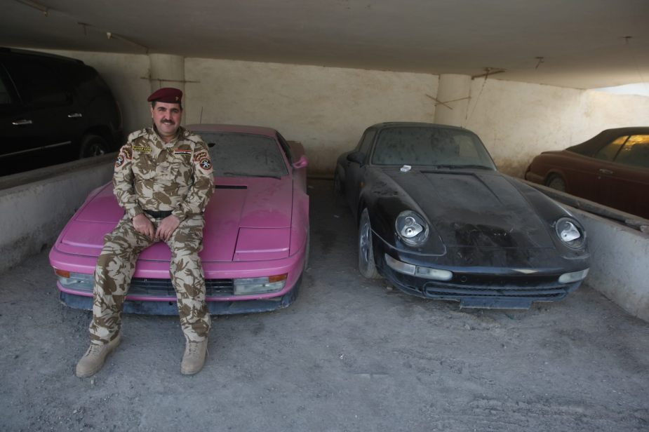 Policeman sits on the hood of a Ferrari Testarossa seized from Uday and Saddam Hussein.