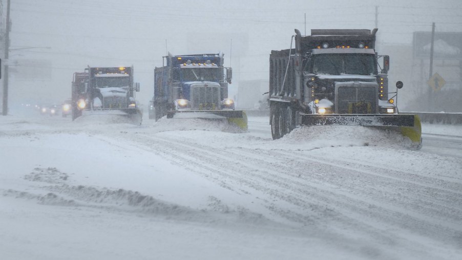 A row of three snowplow trucks clearing a road after a storm.