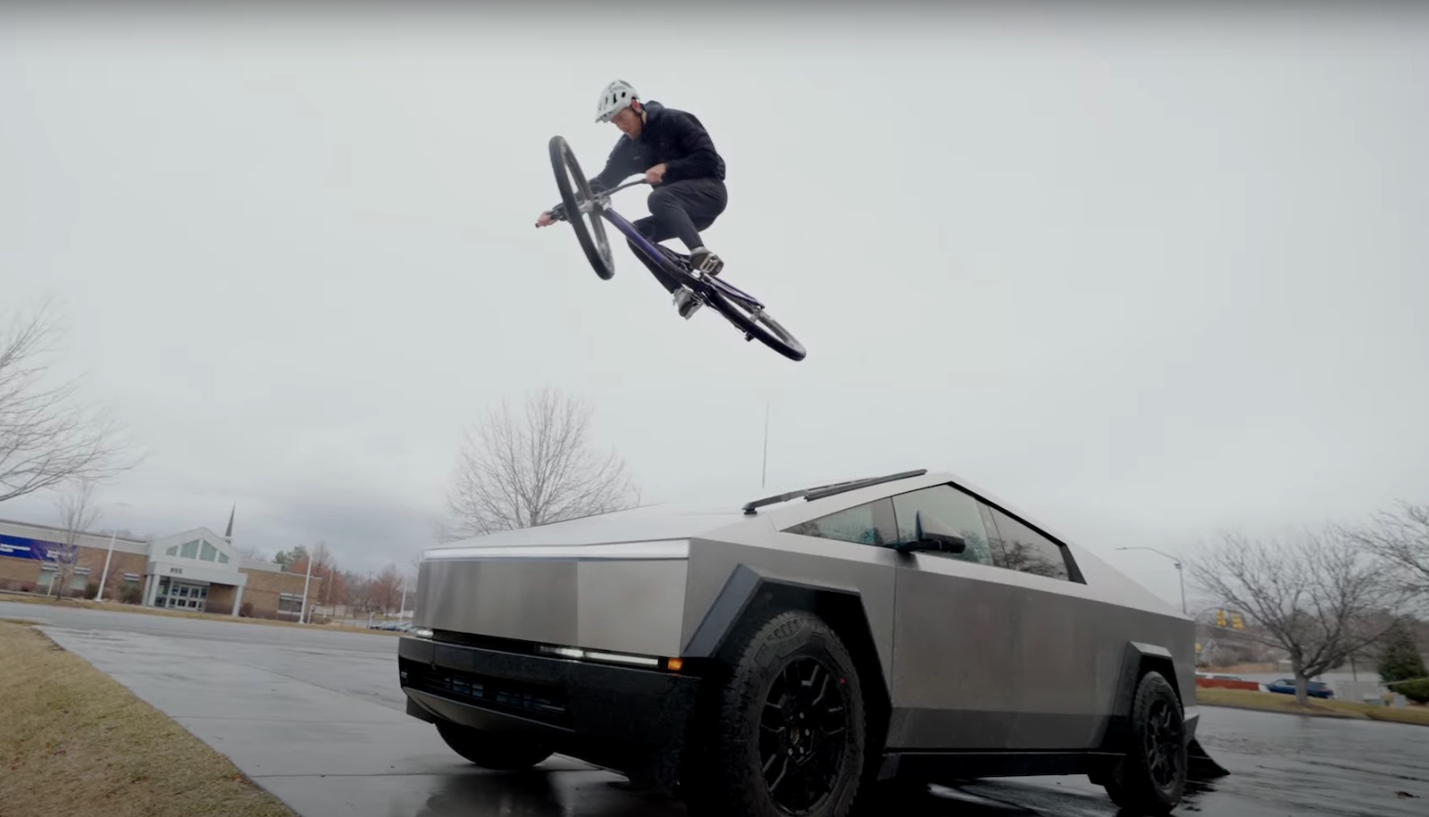 BMX biker jumps off a Tesla Cybertruck in a parking lot.