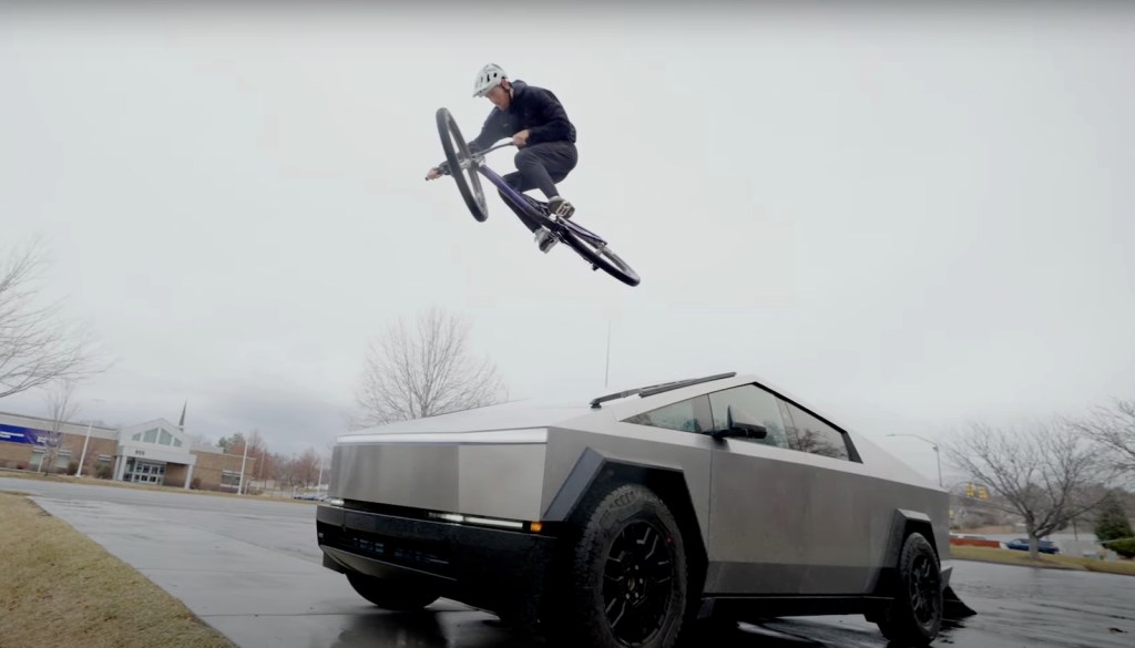 BMX biker jumps off a Tesla Cybertruck in a parking lot.