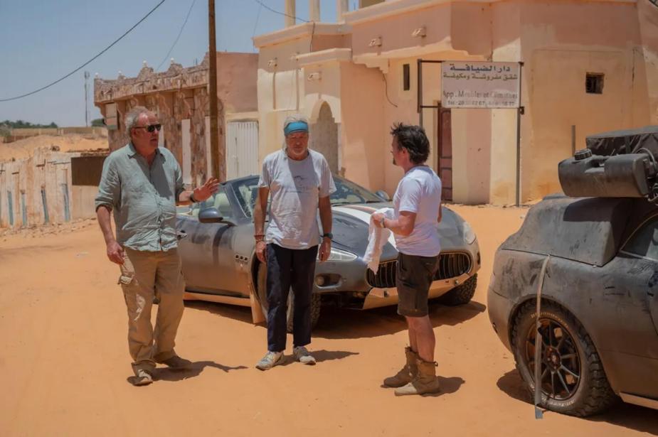 James May, Jeremy Clarkson, and Richard Hammond pose next to a Maserati GranCabrio and an Aston Martin DB9 in Mauritania.
