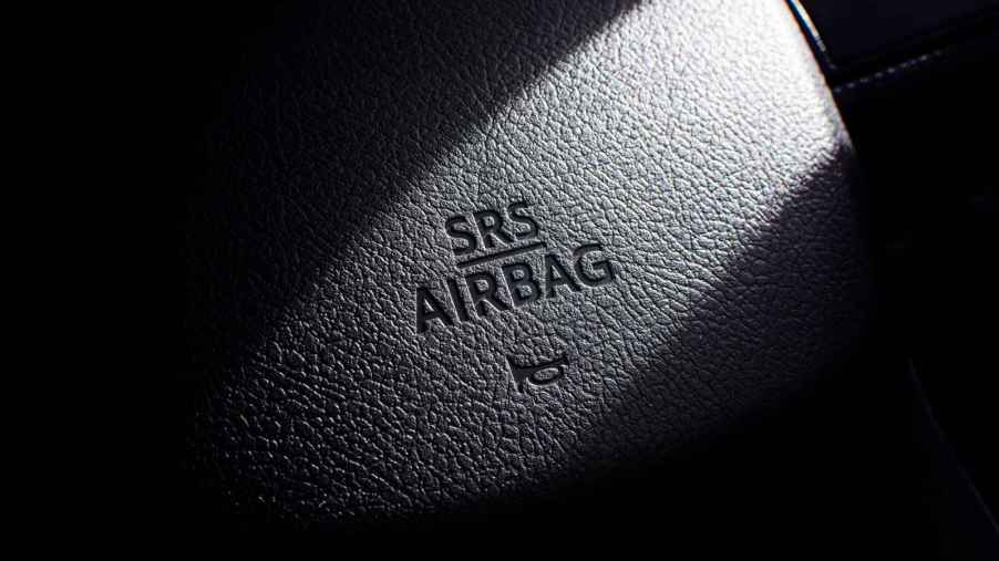 A close view of a black car steering wheel horn with words "SRS AIRBAG" and a car horn icon