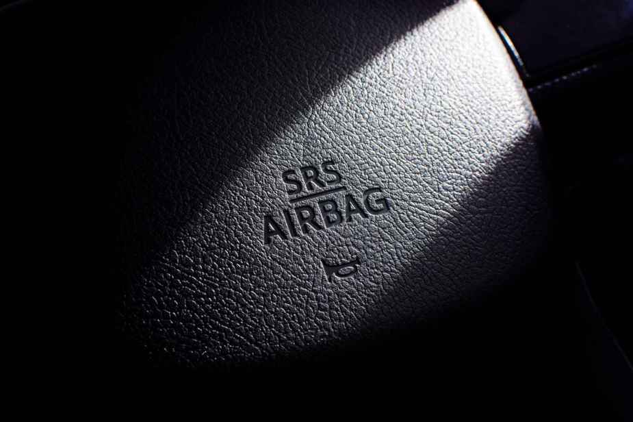 A close view of a black car steering wheel horn with words "SRS AIRBAG" and a car horn icon
