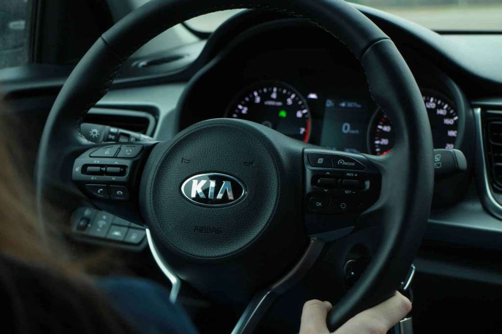 A black Kia steering wheel is shown in slight right front angle with instrument cluster in background