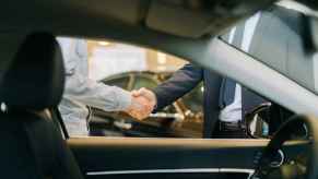 Two men shaking hands shown through a left front car window as the image frame in a luxury car showroom