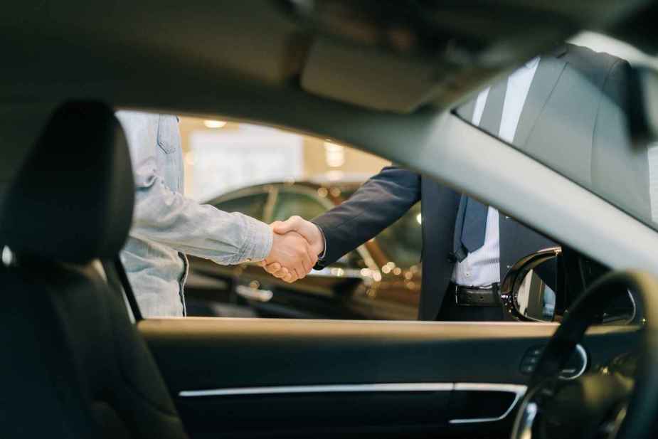 Two men shaking hands shown through a left front car window as the image frame in a luxury car showroom