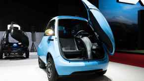 A blue Micro Microlino Lite NEV car with Isetta-like open front door is parked on display
