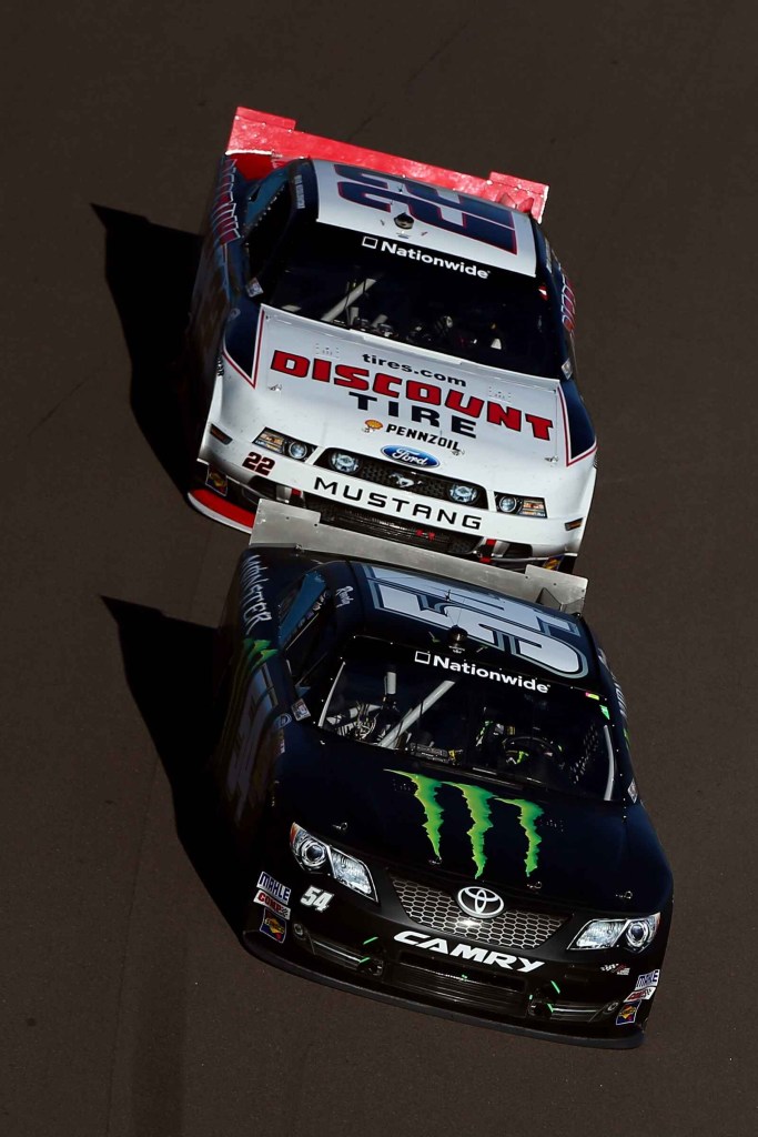 A white NASCAR race car tandem drafts a black Monster Energy Drink NASCAR car in 2013
