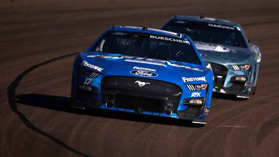 A blue Ford Mustang NASCAR car races in front of a another blue Ford NASCAR car