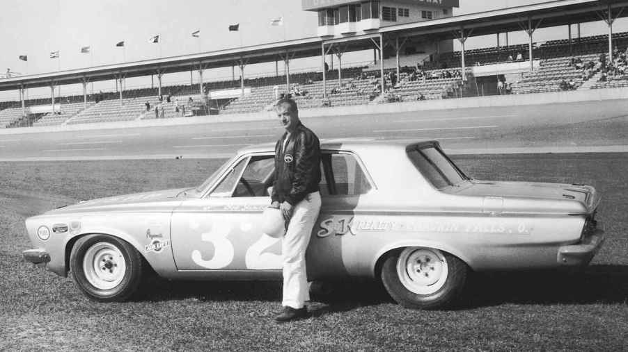 A photo of Bob James at the NASCAR Daytona 500 standing next to a stock 1963 Plymouth.