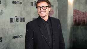 Marvel star Pedro Pascal at a media event wearing all black and black framed glasses with mustache and smiling