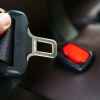 A hand is shown holding up the male end of a car seat belt buckle with red plastic male end in background