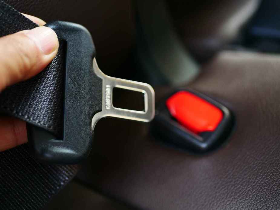 A hand is shown holding up the male end of a car seat belt buckle with red plastic male end in background