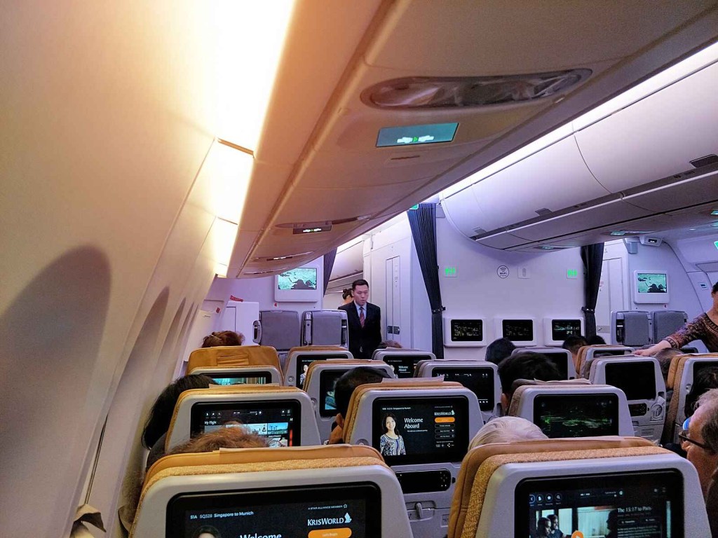 The interior cabin of a Singapore Airlines Airbus A350 is shown with TV screens on the back of seat headrests turned on