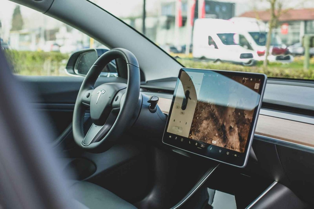 A Tesla front interior is shown with screen display and steering wheel