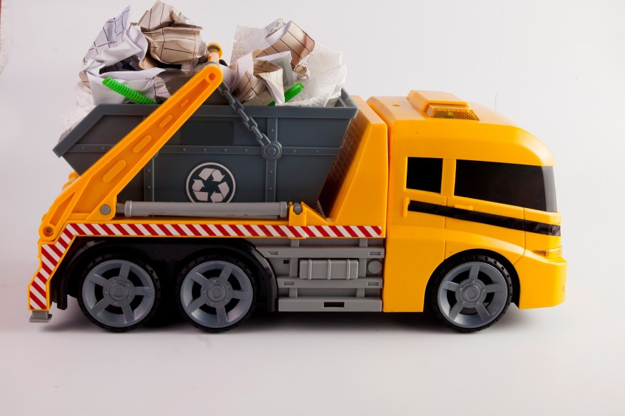 An orange and grey kid's toy garbage truck has crumpled up paper in its bed