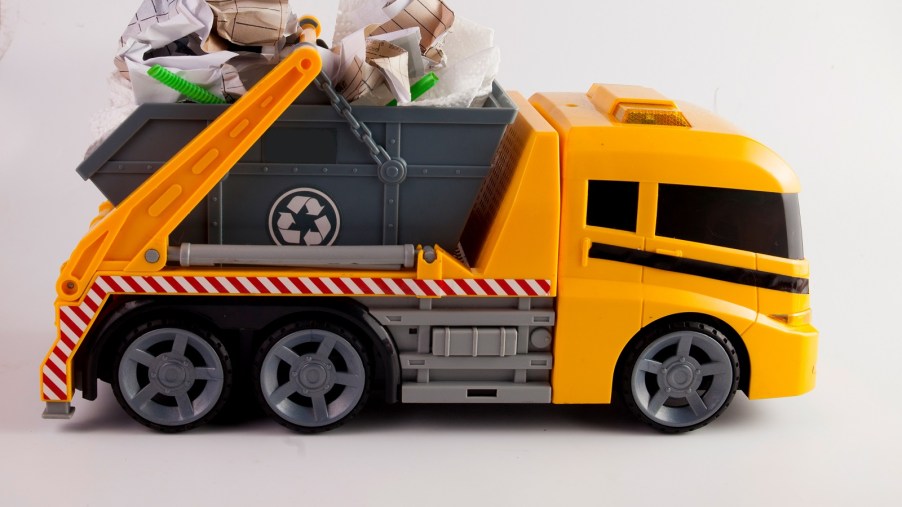 An orange and grey kid's toy garbage truck has crumpled up paper in its bed