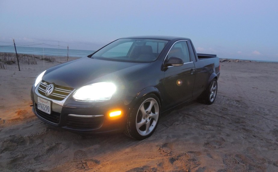 VW Jetta with compact "ute" pickup truck body parked on a beach at dusk, its headlights lit up.
