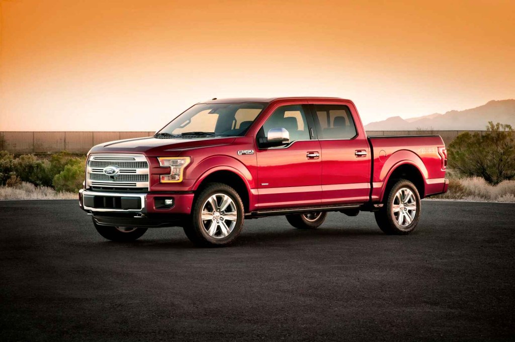 A red 2015 Ford F-150 Platinum is shown parked in left front angle view on black pavement at sunset