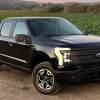 Black 2022 Ford F-150 Lightning electric truck posed next to a field.